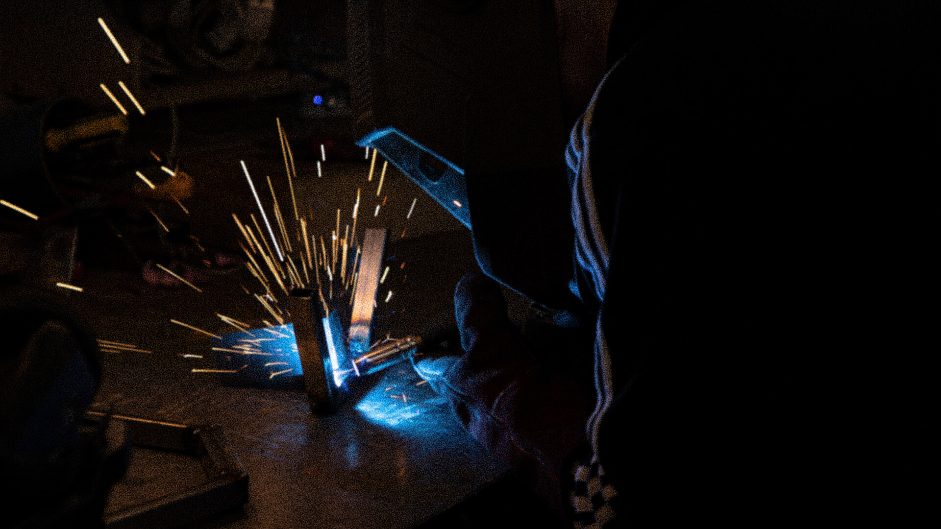 Edinburgh-open-workshop-Master_slide_eow-2-1 Sparks fly as person in protective mask welds metal